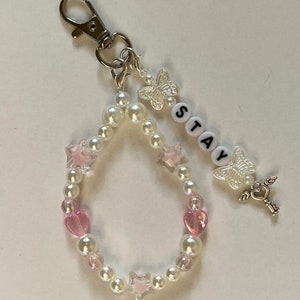 May include: A white pearl and pink heart charm keyring with a silver key charm, a butterfly charm, and the word "STAY" spelled out in white beads.