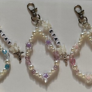 May include: Three pearl beaded keychains with silver key charms and butterfly accents. Each keychain features the word "STAY" spelled out in white letter beads.