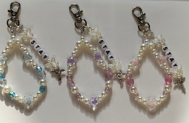 May include: Three pearl beaded keychains with silver key charms and butterfly accents. Each keychain features the word "STAY" spelled out in white letter beads.