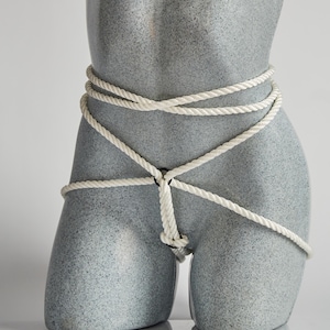 May include: A gray mannequin torso with a white rope tied around the waist and hips. The rope is tied in a knot at the front and is wrapped around the body several times.
