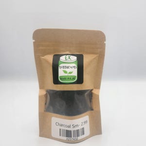 May include: A kraft paper bag with a clear window containing charcoal. The bag has a label with the text "EK Terrariums" and "Nature in a Jar". A smaller label at the bottom reads "Charcoal Sm-".