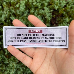 A rectangle die cut sticker of a warning sign with the message NOTICE, DO NOT FEED THE MACHINE, LEST OUR ART BE DONE BY ALGORITHMS AND OUR PASSIONS SQUASHED FOR PROFITS.