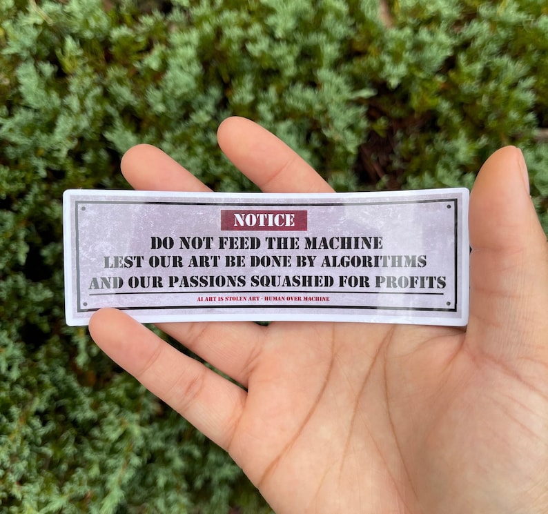 A rectangle die cut sticker of a warning sign with the message NOTICE, DO NOT FEED THE MACHINE, LEST OUR ART BE DONE BY ALGORITHMS AND OUR PASSIONS SQUASHED FOR PROFITS.