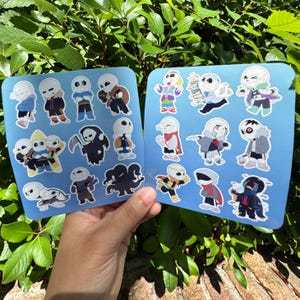 May include: Two light blue sticker sheets featuring various cartoon skeleton characters in different outfits and poses. The characters have white skulls, black eye sockets, and expressive features, displayed in a grid layout on each sheet.