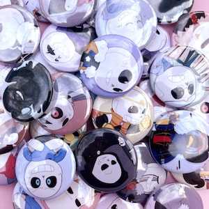 May include: A collection of colorful round buttons featuring various cartoon characters. The buttons are made of metal with a glossy finish. The characters are depicted in different poses and expressions.