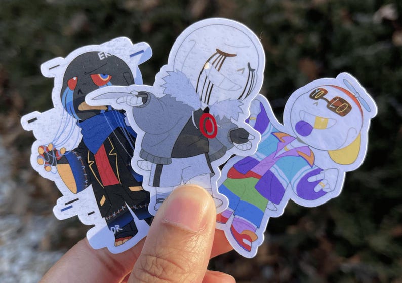 Three skeletons. The one on the left is a black skeleton is string on his hands, the one in the middle is shrugging as he holds a knife, and the one on the left is holding his hands out in upside down peace signs.