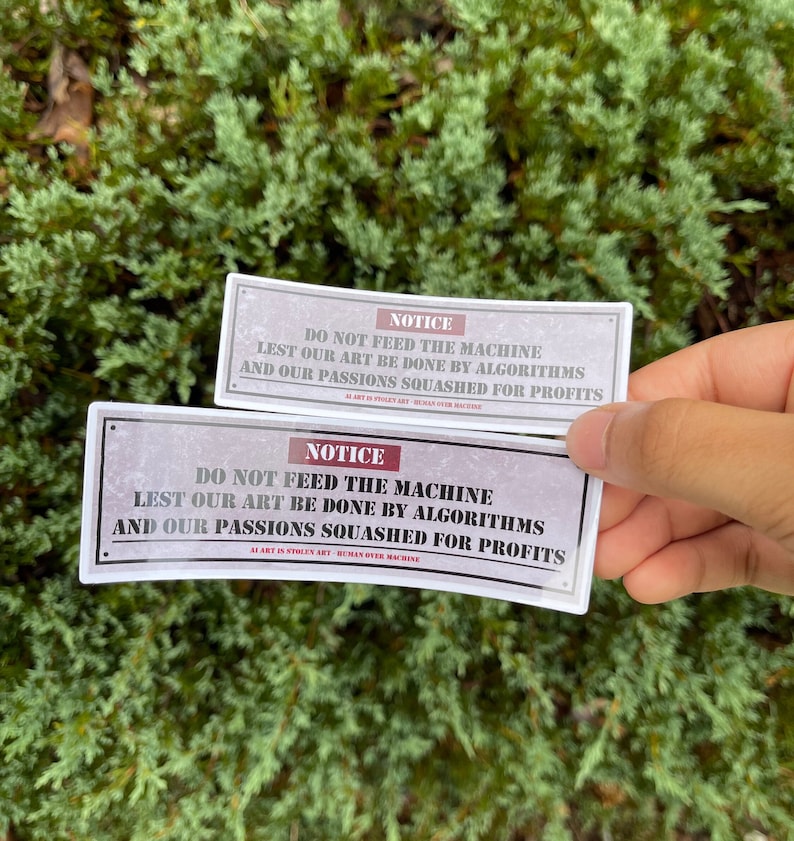 A rectangle die cut sticker of a warning sign with the message NOTICE, DO NOT FEED THE MACHINE, LEST OUR ART BE DONE BY ALGORITHMS AND OUR PASSIONS SQUASHED FOR PROFITS.