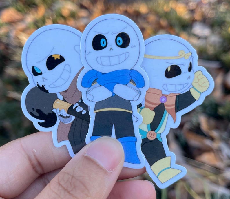 Three skeletons. The one on the left is holding a paint brush, the one in the middle has his arms crossed, and the one on the right has a fist in the air.
