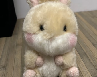 May include: A small, plush, cream-colored bunny with pink ears and paws. The bunny has black eyes and a white belly.