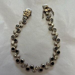 May include: Silver bracelet featuring alternating black and clear gemstones. The bracelet has a delicate design with a secure clasp. The gemstones are round and set closely together, creating a sparkling effect.