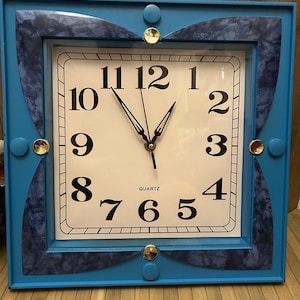 May include: A blue square clock with gold accents and a white face. The clock face has black numbers and hands. The clock says "QUARTZ" at the bottom.