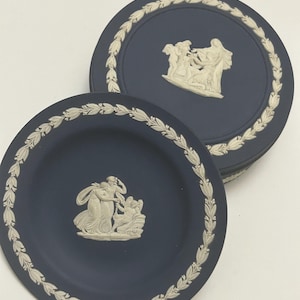 Könnte beinhalten: Zwei blaue und weiße Keramikteller mit einem weißen Blumenrand und einem weißen Reliefdesign von Figuren in der Mitte.