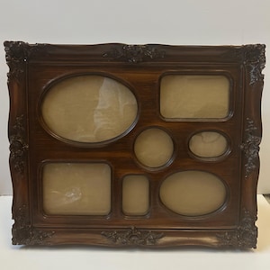 May include: A dark brown, multi-photo frame with various sized openings. The frame has an ornate, carved design around the edges and includes oval, rectangular, and circular openings for photos. The frame is made of wood and has a glossy finish.