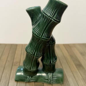 以下が含まれることがあります： 緑色のセラミック製の竹の彫刻。彫刻は、絡み合った2本の竹の茎を特徴としています。竹の茎は濃い緑色で、詳細な溝があります。彫刻は緑色の台座の上にあります。