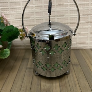 May include: A silver sugar dispenser with a green glass liner and a decorative handle. The dispenser has a cut-out design and sits on three small feet.