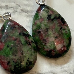 May include: A pair of teardrop-shaped earrings with green, pink and black marbled stone accents. The earrings are made with silver-toned metal.