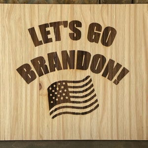 May include: A wooden sign with the text "Let's Go Brandon!" in brown lettering. An American flag is depicted below the text.