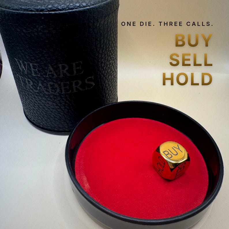 K&ouml;nnte beinhalten: Ein schwarzer, texturierter zylindrischer Beh&auml;lter mit dem Text WE ARE TRADERS und ein passendes schwarzes Tablett mit rotem Filzinnenraum. Ein goldfarbener W&uuml;rfel liegt im Tablett mit den W&ouml;rtern BUY, SELL und HOLD. Text: ONE DIE. THREE CALLS. BUY SELL HOLD.