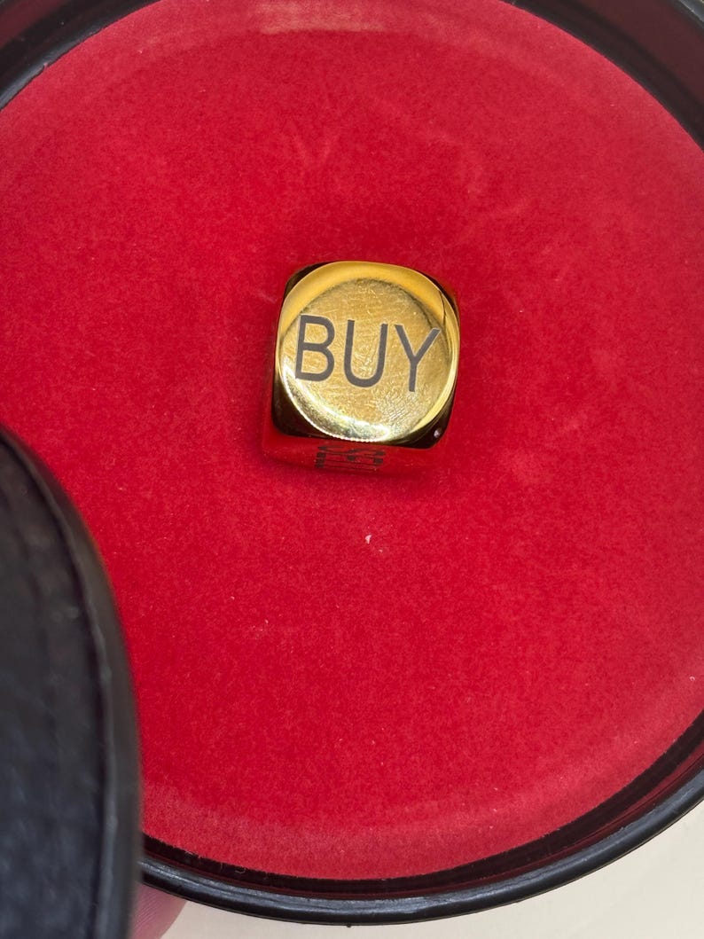 K&ouml;nnte beinhalten: Ein goldfarbener W&uuml;rfel mit abgerundeten Kanten, auf dessen Oberseite das Wort BUY in Schwarz aufgedruckt ist. Der W&uuml;rfel befindet sich in einem runden Beh&auml;lter mit leuchtend rotem Innenfutter und einem schwarzen Au&szlig;enrand.