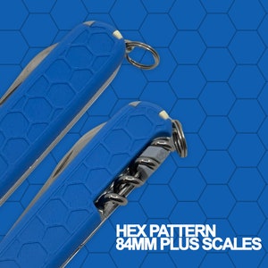 May include: Two blue pocket knives with a hexagonal pattern on the handles. The text "HEX PATTERN 84MM PLUS SCALES" is printed below the knives.