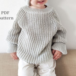 May include: A light gray knitted sweater and matching hat. The sweater has a ribbed texture and long sleeves with flared cuffs. The text "PDF pattern" is visible on the left side of the image. The sweater is paired with light-colored pants.