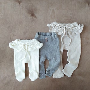 Op de afbeelding: Drie paar gebreide baby leggings met een geruite kraag. Een paar is grijs, een is wit en een is beige.