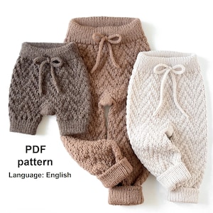 Op de afbeelding: Drie paar gebreide babybroeken in bruin, beige en wit. De broeken hebben een ruitpatroon en een trekkoord.