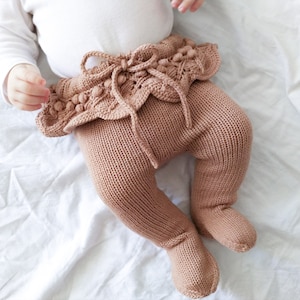 Op de afbeelding: Bruine gebreide baby leggings met een geruite zoom en pompoenen rond de taille.