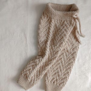 May include: Beige knitted trousers with a chevron pattern and a drawstring waist.
