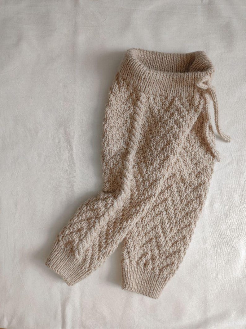 May include: Beige knitted trousers with a chevron pattern and a drawstring waist.