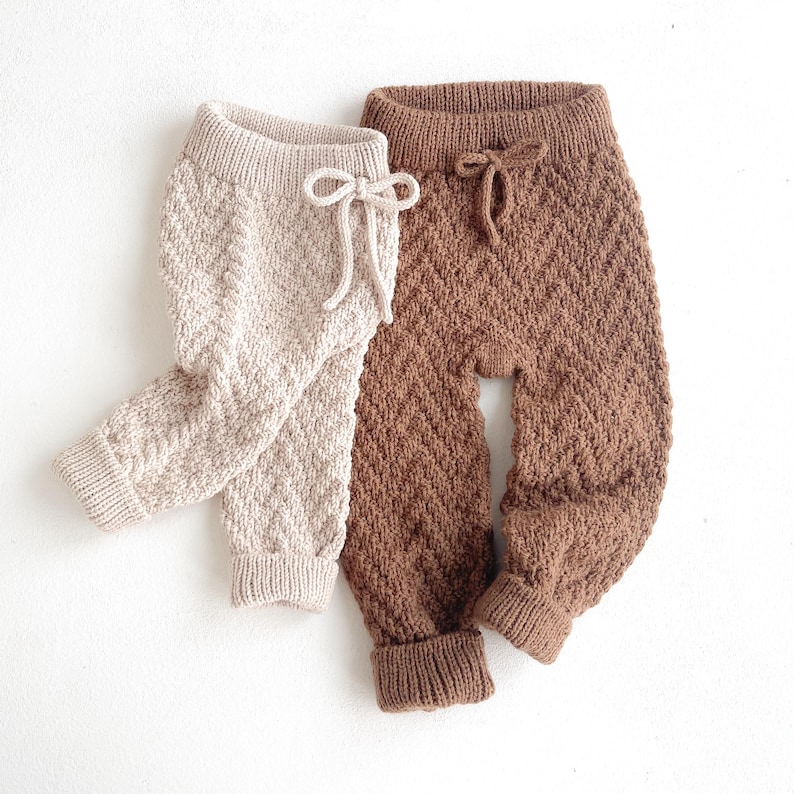 May include: Two pairs of knitted baby trousers. One pair is brown and the other is beige.
