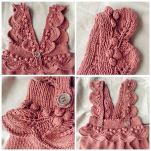 May include: A pink knitted baby romper with a ruffled neckline and straps. The romper has a textured knit pattern and is decorated with small pom-poms.