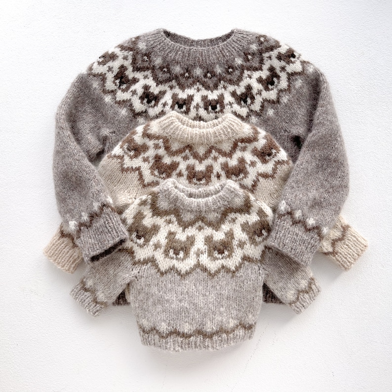 May include: Three brown and white knitted sweaters with a traditional Scandinavian pattern. The sweaters are stacked on top of each other, with the largest sweater on the bottom and the smallest sweater on top.