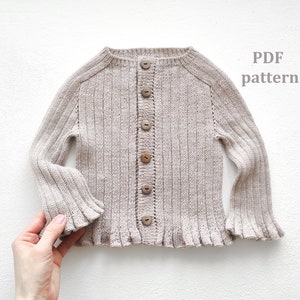 May include: A beige knitted cardigan with a button fastening and ruffled edges. The cardigan is made with a ribbed knit pattern. The text "PDF pattern" is visible in the top right corner of the image.