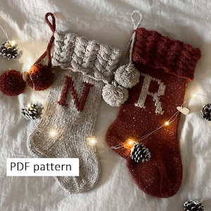 May include: Two knitted Christmas stockings, one gray with a red "N" and the other red with a white "R". Both have braided cuffs, pom-poms, and hanging loops. The text "PDF pattern" is visible.