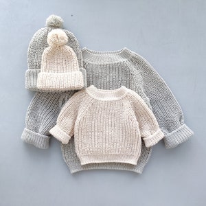 Puede incluir: Dos jers&eacute;is de punto, uno gris y otro crema, con un gorro de punto crema con un pomp&oacute;n blanco.