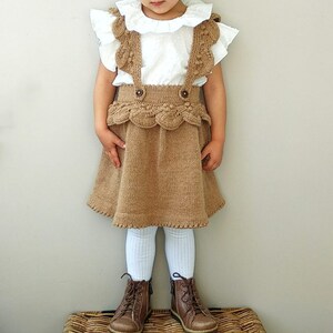 May include: A brown knitted skirt with a scalloped hem and a white ruffled blouse. The skirt has a decorative strap detail and the blouse has a white collar.