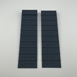 May include: Two dark blue plastic rulers with millimeter markings. The ruler on the left has markings from 1.5 mm to 12.7 mm. The ruler on the right has markings from 1 mm to 10 mm.