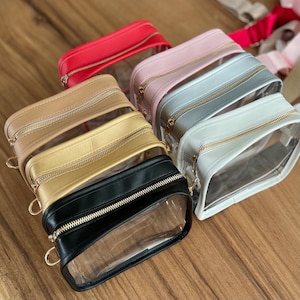 May include: Six clear plastic bags with zipper closures and a leather flap. The bags are in different colors: red, pink, gray, white, gold, and black.