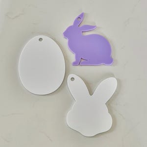 May include: Three flat acrylic shapes including a white oval, a light purple rabbit silhouette, and a white rabbit head silhouette. Each piece features a small circular hole at the top for hanging, providing a smooth surface for crafting projects.