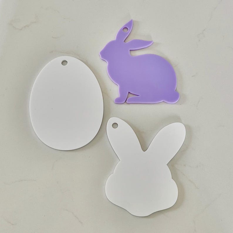 May include: Three flat acrylic shapes including a white oval, a light purple rabbit silhouette, and a white rabbit head silhouette. Each piece features a small circular hole at the top for hanging, providing a smooth surface for crafting projects.