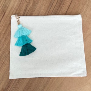 May include: A white canvas pouch with a zipper closure and a turquoise and green tassel attached to the zipper pull.