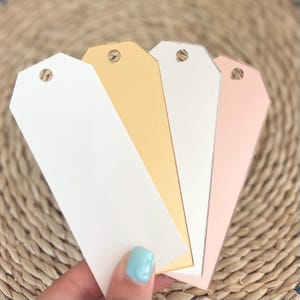 May include: Four blank gift tags in different colors: white, gold, silver, and pink. The tags are made of a sturdy material and have a hole punched at the top for string or ribbon.