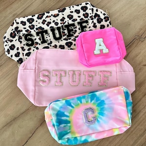 Peut inclure: Quatre trousses de toilette roses et blanches avec des motifs différents. Les trousses portent le mot "STUFF" et les lettres "A" et "C" brodées.