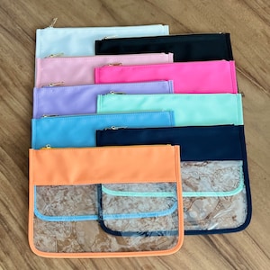 Pode incluir: Uma pilha de dez bolsas com z&iacute;per em v&aacute;rias cores, incluindo azul claro, rosa, lavanda, verde menta, preto e laranja. As bolsas t&ecirc;m janelas de pl&aacute;stico transparente na frente.