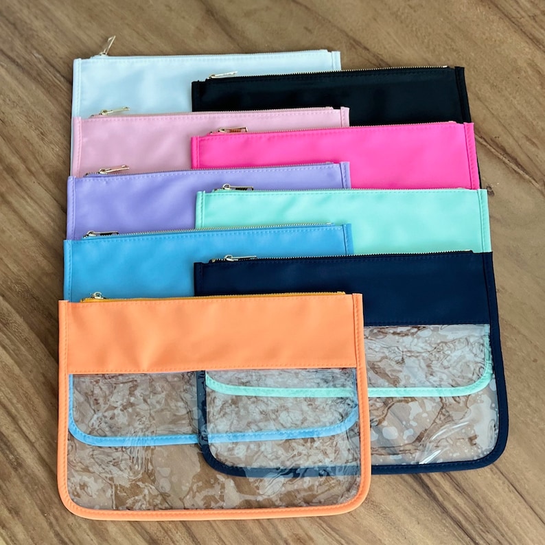 Pode incluir: Uma pilha de dez bolsas com z&iacute;per em v&aacute;rias cores, incluindo azul claro, rosa, lavanda, verde menta, preto e laranja. As bolsas t&ecirc;m janelas de pl&aacute;stico transparente na frente.