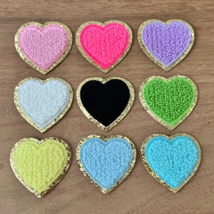 May include: Nine felt heart-shaped patches with gold glitter trim. The hearts are in various colors including pink, red, purple, white, black, green, yellow, light blue, and turquoise.