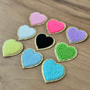 Peut inclure: Huit patchs en forme de cœur avec une texture duveteuse et une bordure dorée pailletée. Les couleurs sont rose, rose vif, blanc, noir, jaune, vert clair, bleu clair et turquoise.