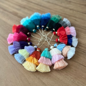 Pode incluir: Uma cole&ccedil;&atilde;o de 18 franjas coloridas em v&aacute;rios tons de azul, verde, vermelho, rosa, roxo, amarelo e branco. As franjas est&atilde;o dispostas em c&iacute;rculo sobre uma superf&iacute;cie de madeira.