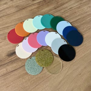 May include: A collection of circular acrylic blanks in various solid colours including red, orange, light green, mint, teal, dark green, light blue, navy, pink, lavender, white, cream, and black, plus gold glitter, silver glitter, and clear discs.